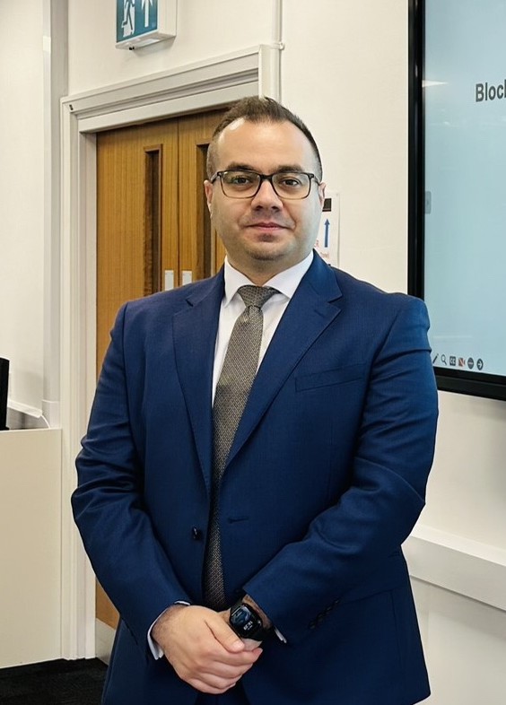 Mohammed wearing a blue suit, white shirt and brown tie pictured from the waist up