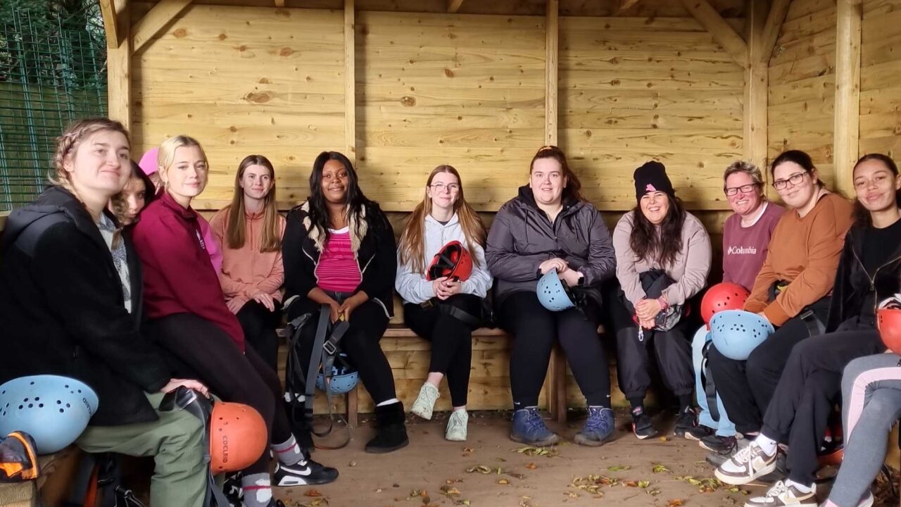 Education students sitting in a shelter holding climbing helmets