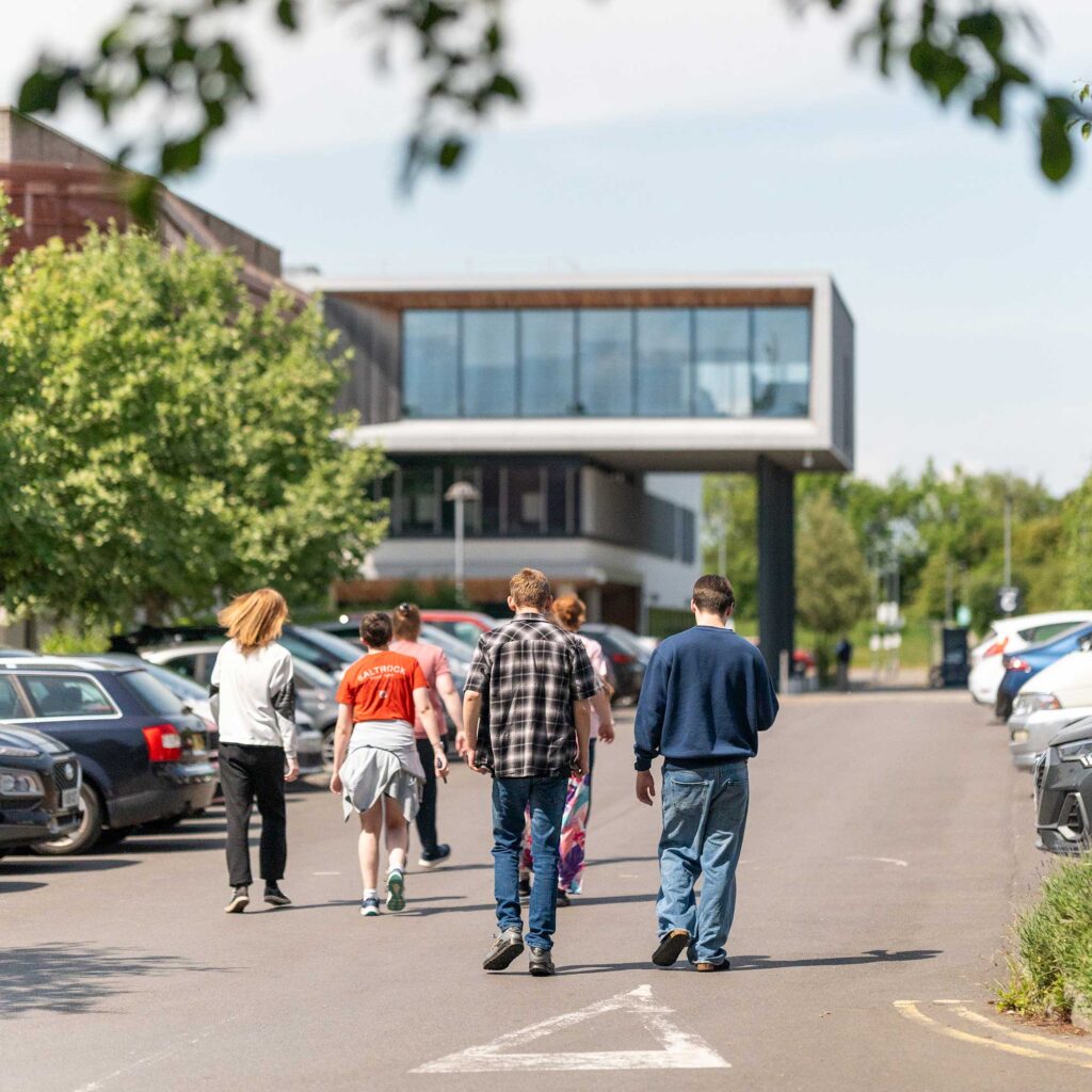A group of students walk through the car park at Oxstalls Campus.