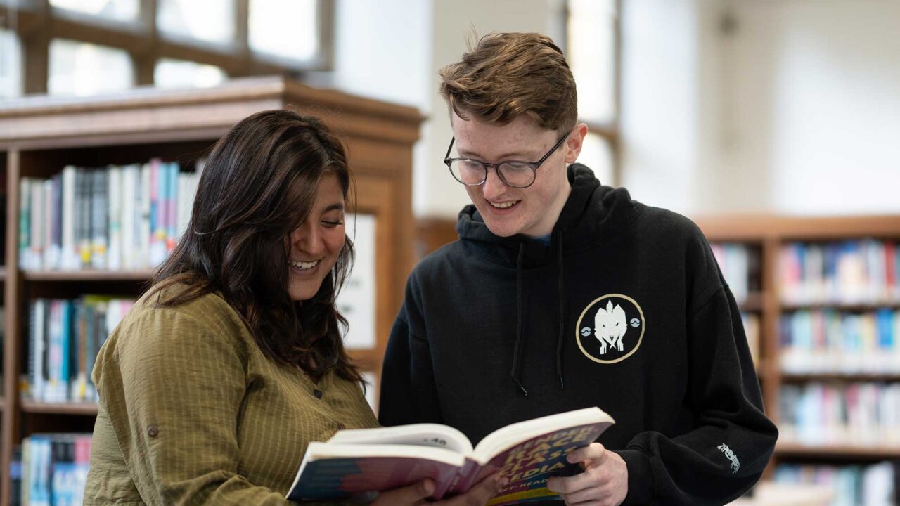 Two students look at a book together in the Francis Close Hall library.