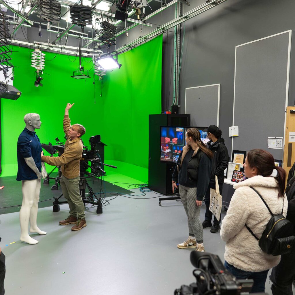 Students look at media campus facilities including a green screen and television equipment.