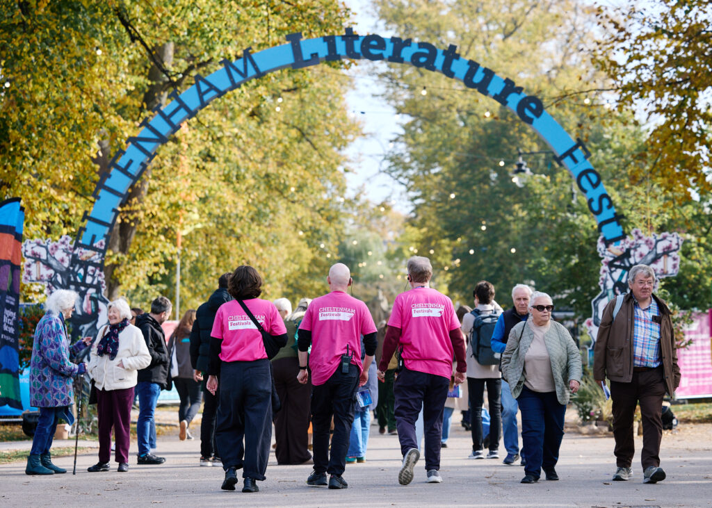 groups of people walking under an arched sign displaying the words Cheltenham Literature Festival