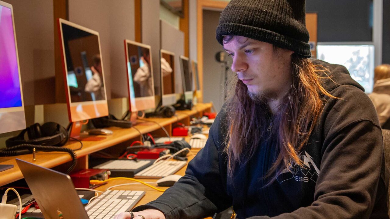 Music student wearing hat works at a laptop.